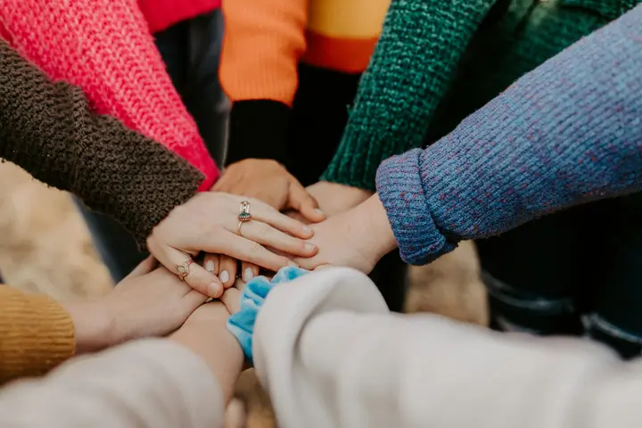 Eight hands in brightly coloured knitted sleeves stacked together in the middle of a circle.